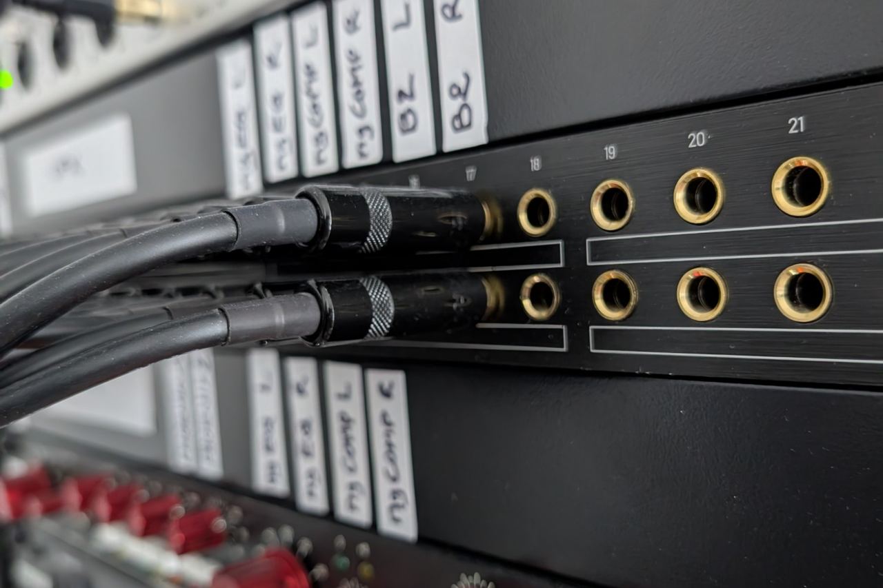 Patch cables in a bay of gold jacks, labelled by hand, above a row of red-knobbed preamps.